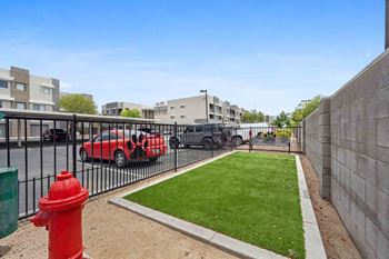 A red fire hydrant is in the foreground of a grassy area with a parking lot and buildings in the background.